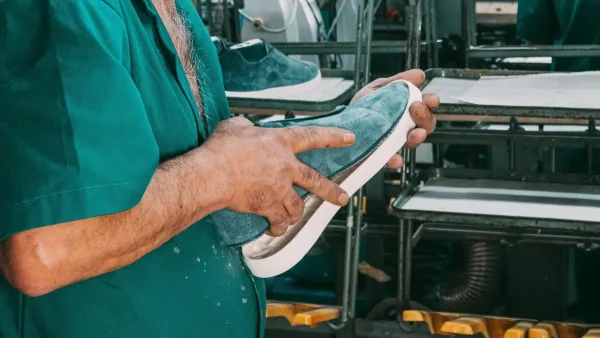LG Shoes - Custom outsole tooling: when should footwear brands invest in a custom sole? 4 A worker’s hands positioning a blue-green shoe upper against a white sole unit at a footwear workbench.